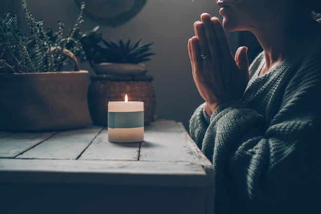 Concept van innerlijke levensbalans en meditatie met vrouw die bidt met gevouwen handen voor een vuurkaars thuis in het donker mensen bidden en mediteren welzijn in alternatieve levensstijl vrouw