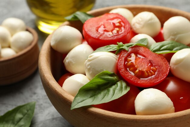 Concept van lekker eten met kom mozzarella, tomaat en basilicum op grijze tafel