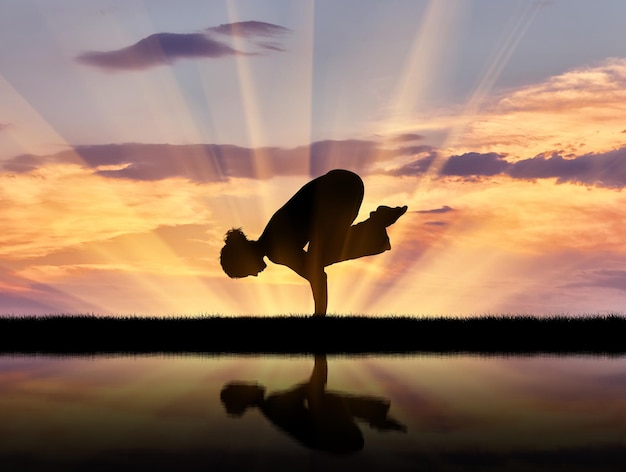 Concept van meditatie en ontspanning. Silhouet van een meisje dat yoga beoefent bij zonsondergang en reflectie in water