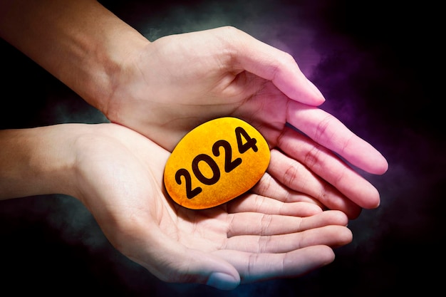 Concept van Nieuwjaar 2024 Afbeelding van een hand die een stenen kiezelsteen vasthoudt met de nieuwe jaarnummers van 2024
