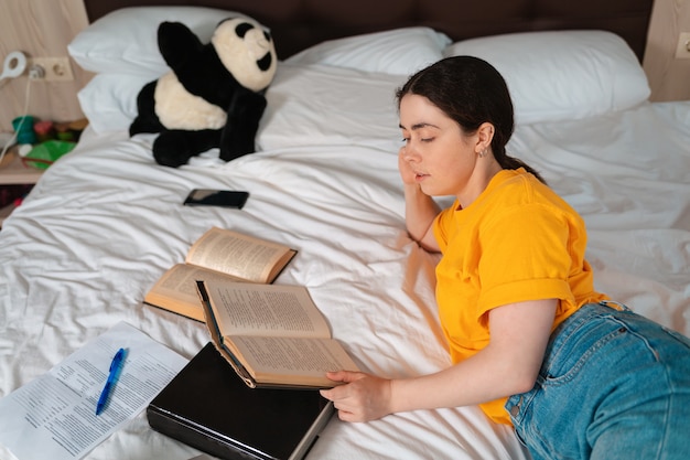 Concept van onderwijs en vrije tijd. Mooi meisje dat op een bed ligt en een boek leest. Bovenaanzicht.