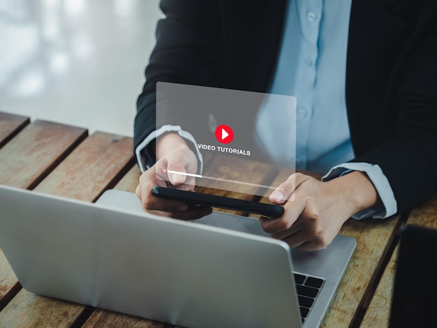 Concept van online video-tutorial Rood afspeelpictogram op virtuele schermweergave van video-tutorial op mobiele smartphone tijdens het gebruik van laptopcomputer kijken door zakenvrouwonderwijs e-learning op internet