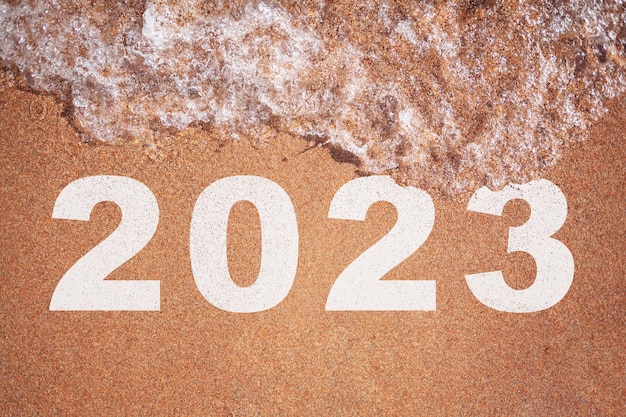 Concept van plannen voor 2023. Een golf van water spoelt het cijfer 2023 weg op het zand aan de kust