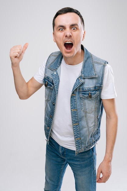 Concept van rockster. Mid-air shot van knappe jonge man met denim kleding springen en gebaren op een witte geïsoleerde achtergrond.