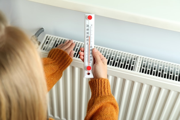 Concept van stookseizoen met meisje houdt thermometer in de buurt van radiator.