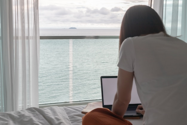 Concept van werkvrouwen werken op laptop in een hotelkamer met uitzicht op zee