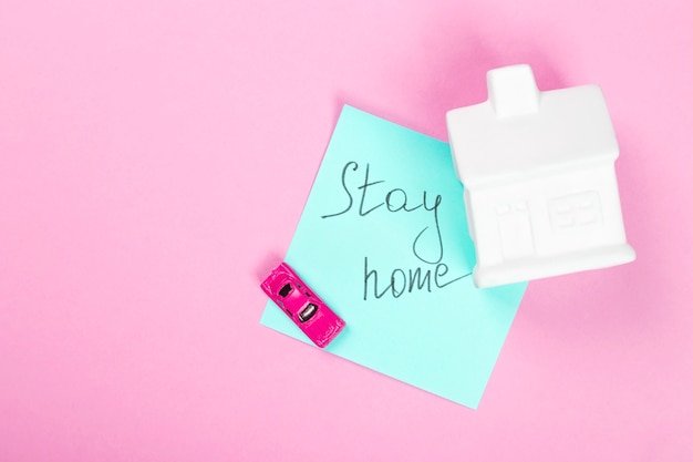 Concept van zelfisolatie en quarantaine. blijf thuis. witte huis, speelgoedauto en sticker met tekst op roze achtergrond. kopieer ruimte