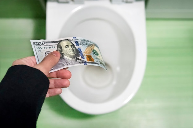 Concept van zinloze verspilling van geld, verlies, nutteloos afval, grote waterkosten, 100 dollarbiljetten die in een toiletpot worden gespoeld. geld verliezen, geld verliezen