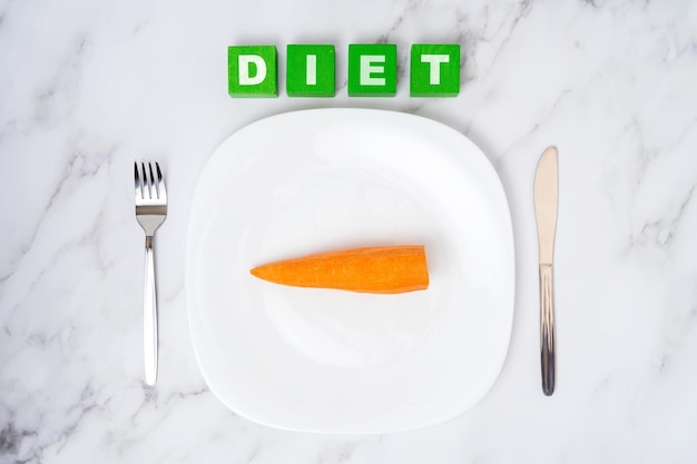 The concept of a vegetable diet An empty white plate with a carrot on a white marble background