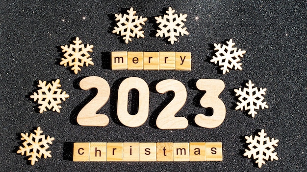 Concept voor Kerstmis en Nieuwjaar houten sneeuwvlokken nummers 2023 en de inscriptie HAPPY CHRISTMAS van houten letters op zwarte glinsterende sterrenhemel achtergrond kerstkaart kerstavond nacht
