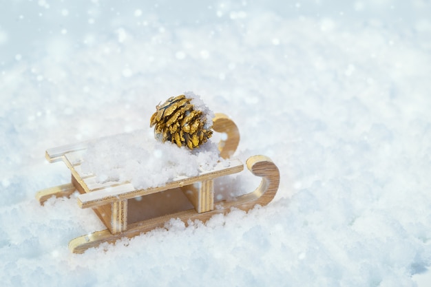 Concept voor Nieuwjaar en Merry Christmas van houten slee en gouden dennenappel op sneeuw