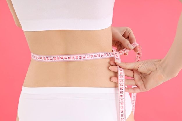 Concept of weight loss with slim young woman on pink background