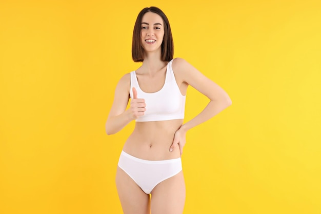 Concept of weight loss with slim young woman on yellow background