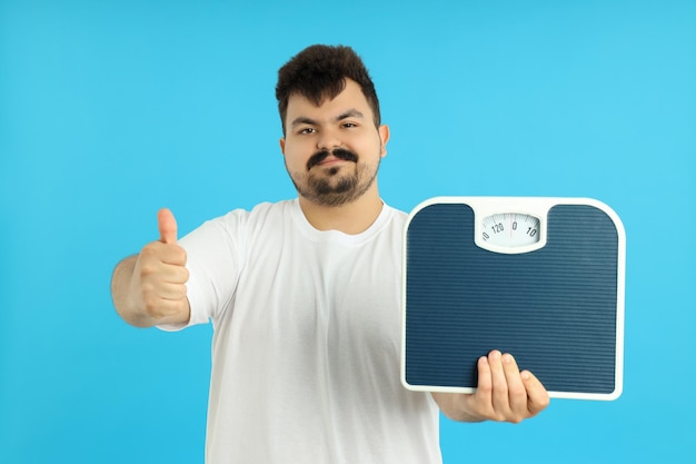 Concept of weight loss young man with scales on blue background