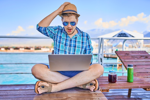 Concept werk op vakantie man zit op de pier en kijkt naar de laptopcomputer freelancer in...