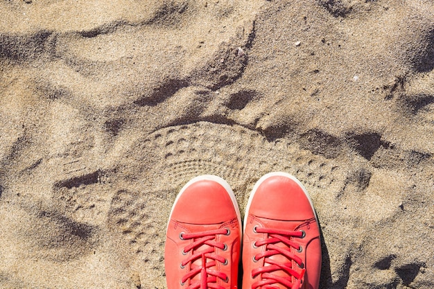 Concept with pink sneakers on bright sea sand. Summer vacation background with space for the text.