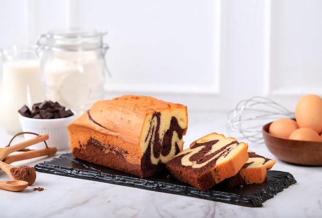 Concept witte achtergrond bakkerij, loaf marble cake slice op stenen zwarte plaat met ingrediënt op achtergrond