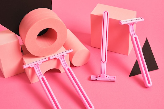 Concetto di cura del corpo femminile. vari stand e podi geometrici e diversi rasoi rosa su sfondo rosa. arte del femminismo