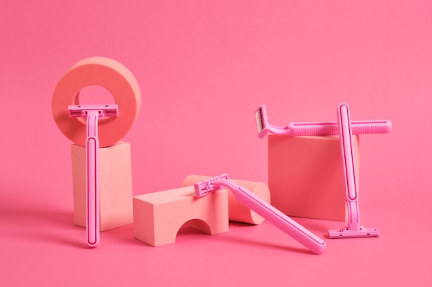 Concept of women's body care. various geometric stands and podiums and several pink razor on a pink background.