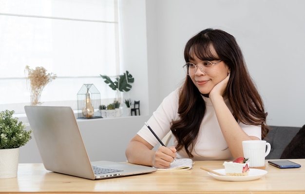 Фото Концепция работы дома азиатская женщина сидит и смотрит на экран. готов писать на бумаге с намерением это новая нормальная трудовая жизнь