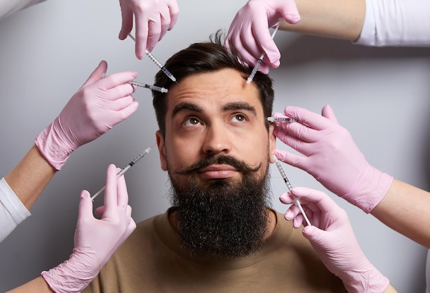 Photo conceptual beauty and cosmetology image of hands of several doctors holding syringes over male face