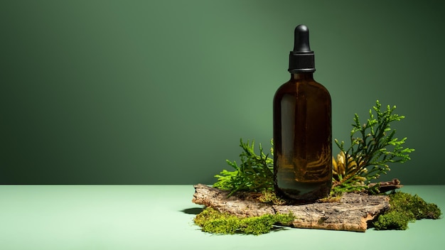 A conceptual composition of essential oil moss and tree bark on a green background Oil with serum for skin and hair care Glass bottle of body oil with a dropper Selfcare and wellness Copy space