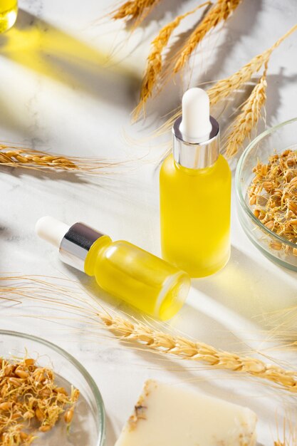 Composizione concettuale di oli essenziali di grano e germe di grano su un tavolo di marmo olio con siero per la cura della pelle e dei capelli bottiglie di olio per il corpo con una pipetta trattamento biologico benessere selfcare