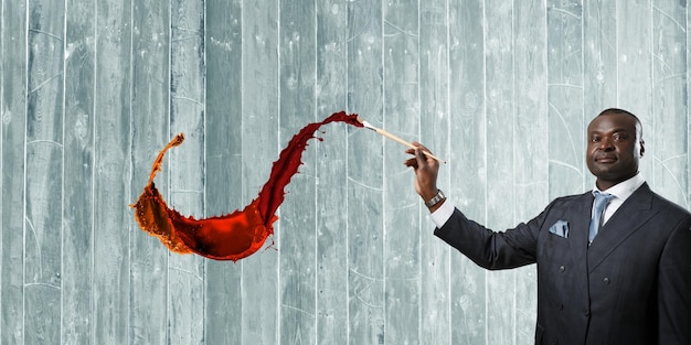 Conceptual image of ambitious and creative businessman in black suit holding paintbrush in hand