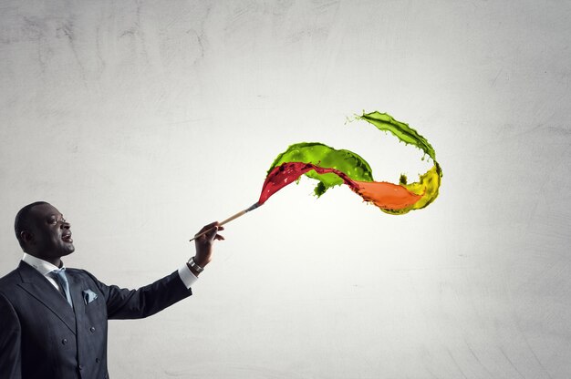 Conceptual image of ambitious and creative businessman in black suit holding paintbrush in hand