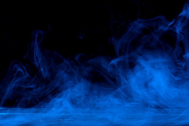 暗い黒の背景と木製のテーブルに分離された青い煙の概念的なイメージ