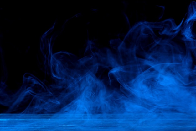 暗い黒の背景と木製のテーブルに分離された青い煙の概念的なイメージ