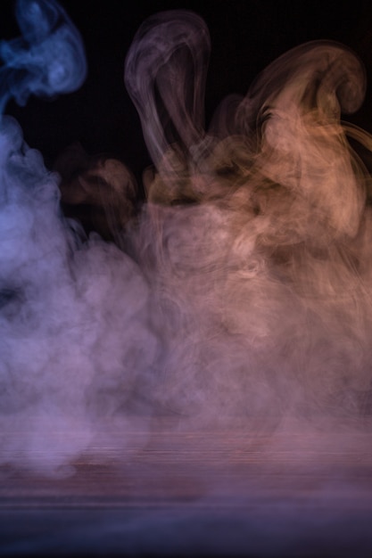 Photo conceptual image of multi-colored smoke isolated on dark black background and wooden table.