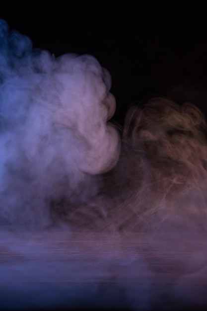 Conceptual image of multicolored smoke isolated on dark black background and wooden table