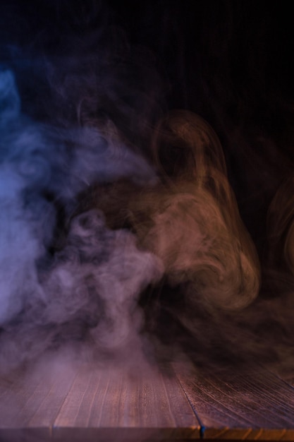 Conceptual image of multicolored smoke isolated on dark black background and wooden table