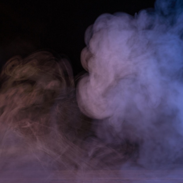 Conceptual image of multicolored smoke isolated on dark black background and wooden table