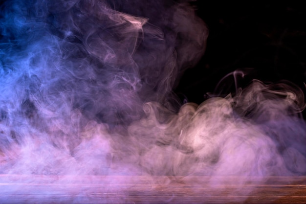 Conceptual image of multicolored smoke isolated on dark black background and wooden table