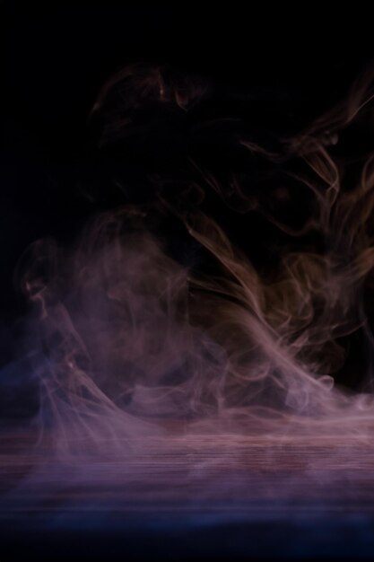 Conceptual image of multicolored smoke isolated on dark black background and wooden table