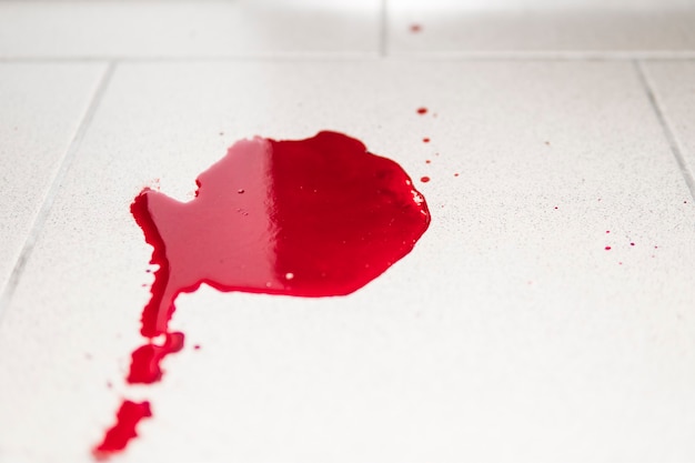 Conceptual image with blood on it resting on tiles on the floor. A puddle of dried blood on the tiled bathroom floor.