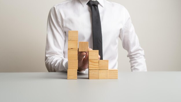 Conceptual image with businessman supporting one step in a staircase made of wooden blocks with his finger