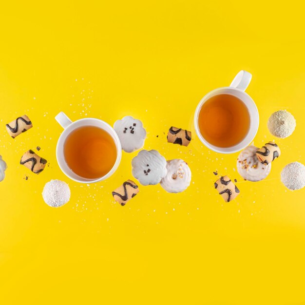 Conceptual photo flying cookies and two cups of tea on a yellow backgroundcopy space