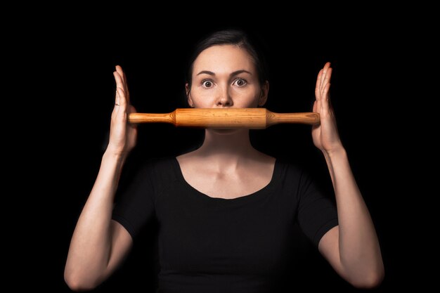 Conceptual photo with a girl and a rolling pin. Girl closes her mouth with a rolling pin. A woman in an everyday household routine. Helping defenseless women in families