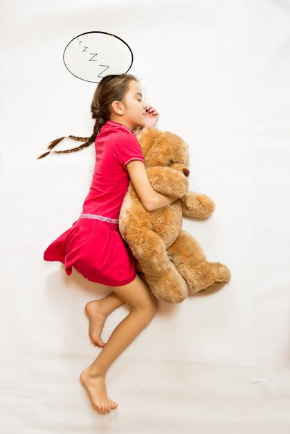 Conceptual shot from top view of cute dreaming girl lying on big teddy bear