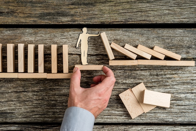 Conceptueel van levensverzekeringen met de hand van een man die via een stabiel platform steun biedt aan een papieren man die de ineenstorting stopt die wordt veroorzaakt door houten stenen.