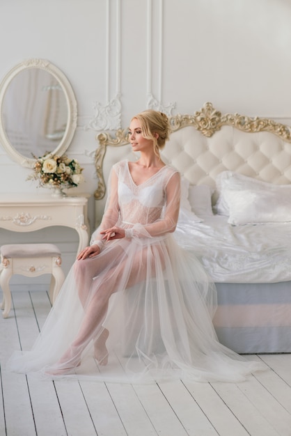 Conceptuele bruiloft, de ochtend van de bruid in de Europese stijl. Boudoir-jurk, kosten in de binnenkamer. Wit minimalisme voor de bruid