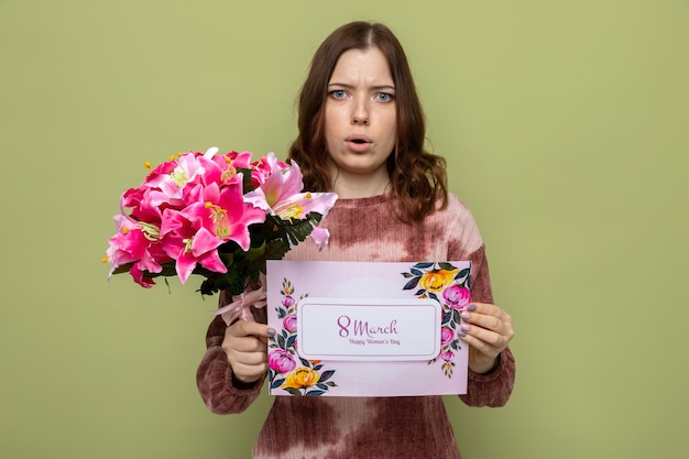 Concerned beautiful young girl on happy women's day holding bouquet with greeting card 