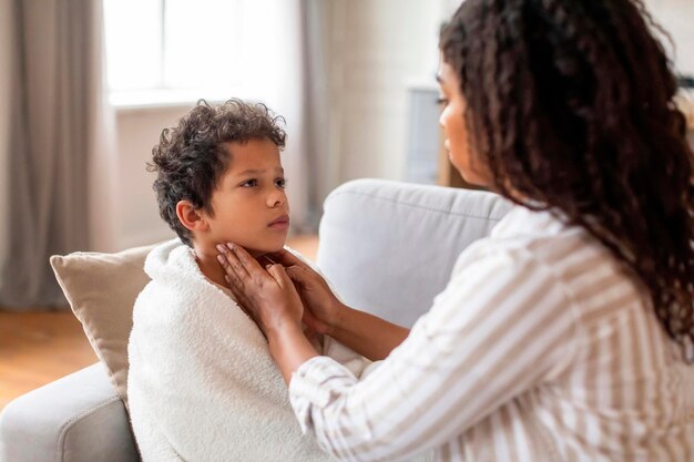 Photo concerned black mother gently touching her sons throat checking signs of illness