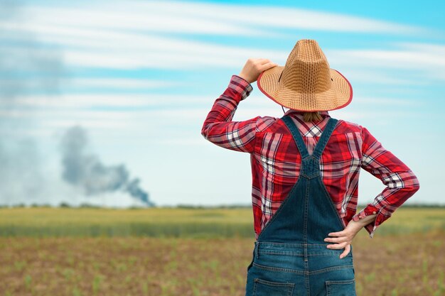 Concerned female farmer in corn field looking at black smoke on horizon