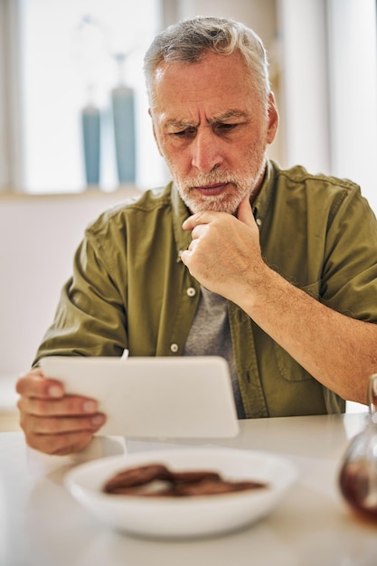 Photo concerned senior citizen checking updates on his tablet