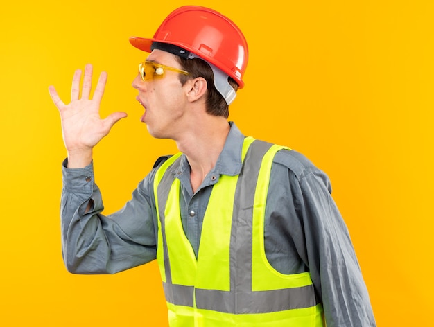 Preoccupato in piedi nella vista di profilo giovane uomo costruttore in uniforme con gli occhiali che chiama qualcuno