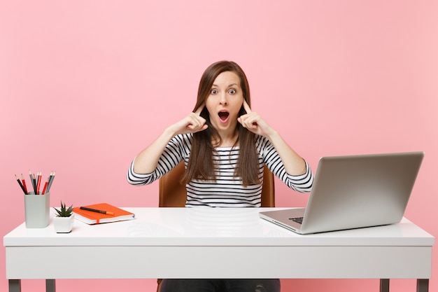 Concerned woman does not want to listen covering ears with fingers sit and work at white desk with contemporary pc laptop